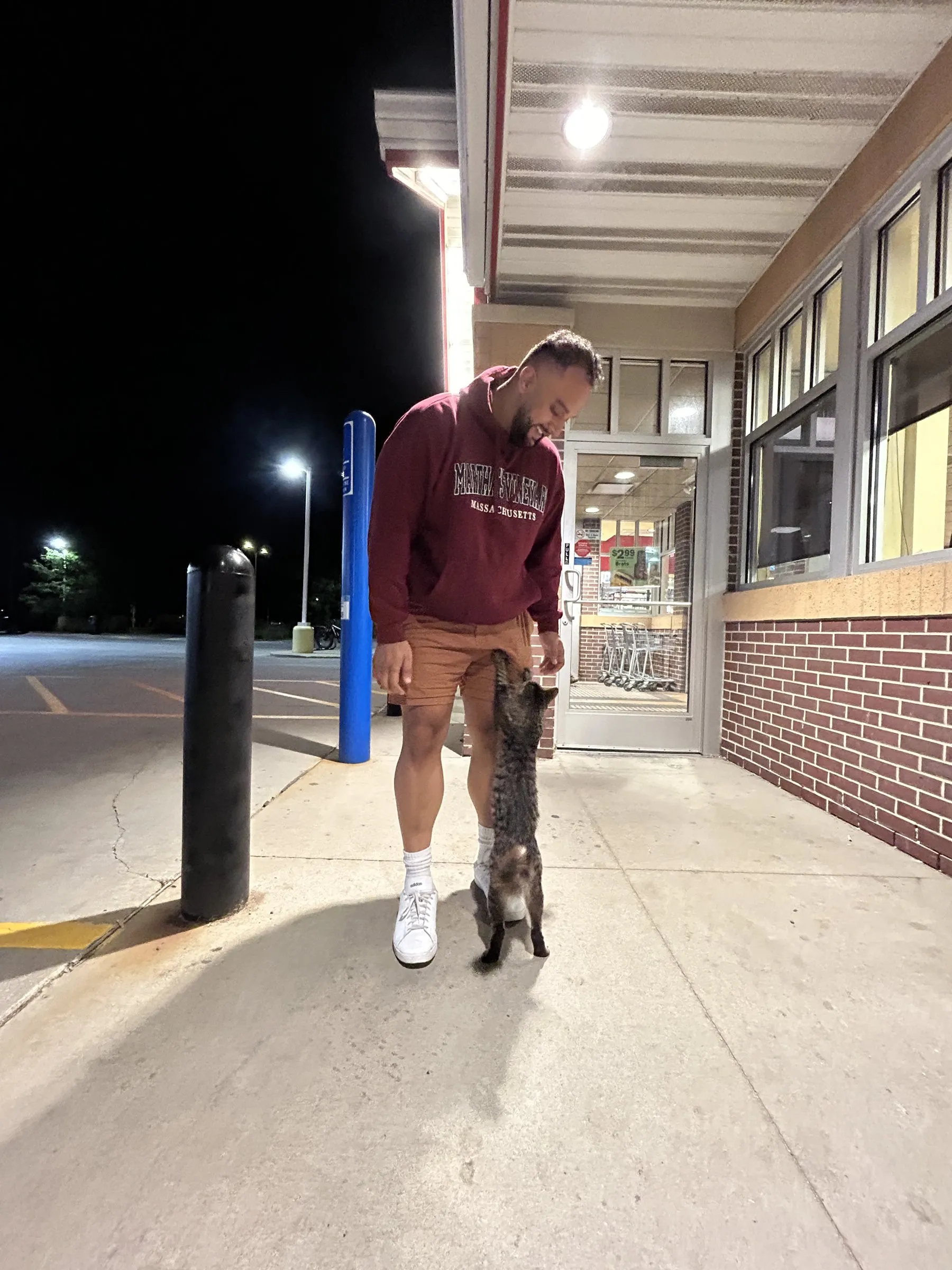 Addy laughing at night outside a store while a stray cat stretches up his leg